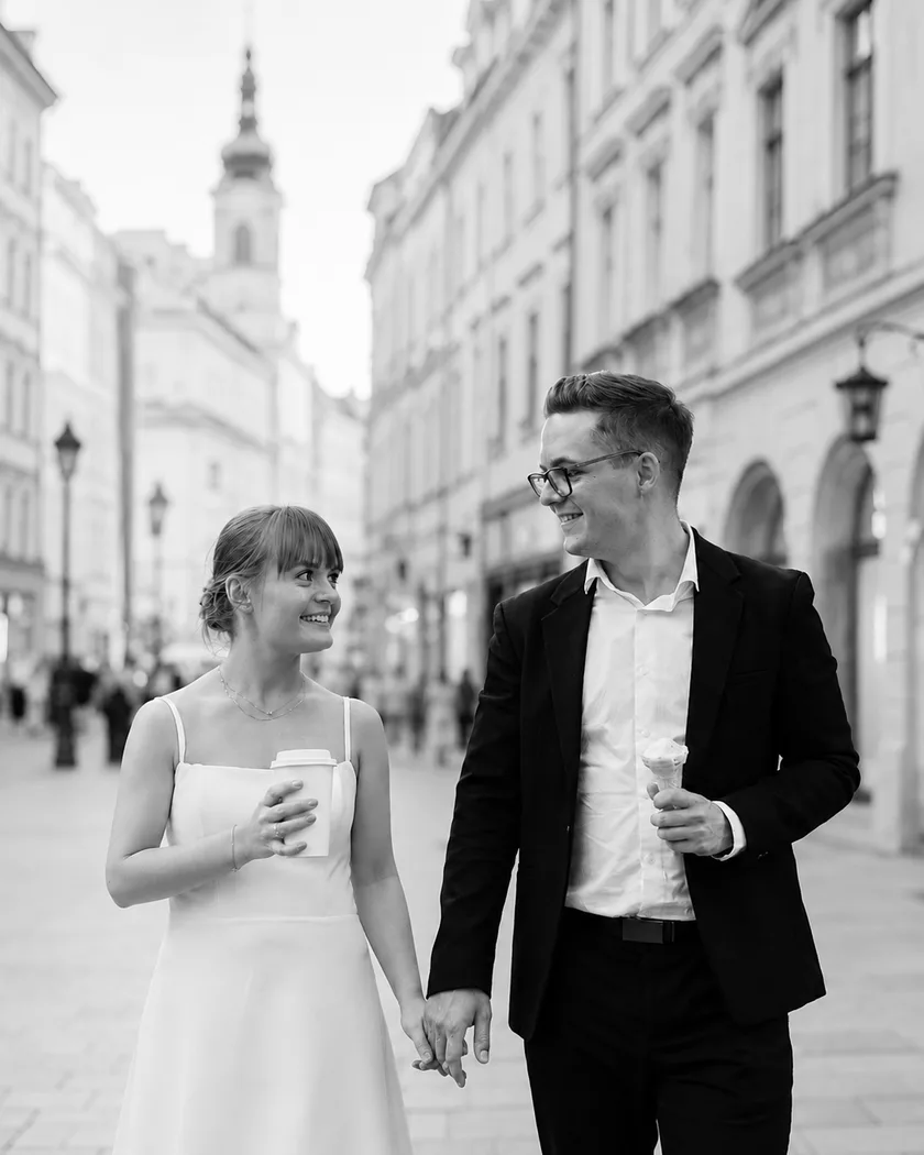 Oliwia i Arek - założyciele The Wedding Post, idą za rękę ulicą starego miasta, z kawą i lodami w dłoniach, i uśmiechają się do siebie